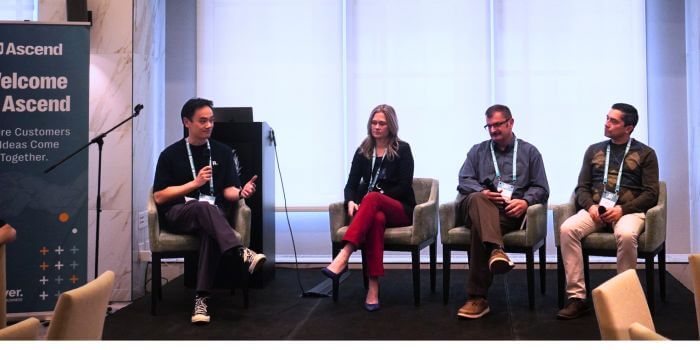 A panel of four professionals seated on stage during a discussion at ascend grc day in toronto. One panelist speaks into a microphone while the others listen. A nearby banner reads “welcome to ascend – where customers & ideas come together. ”