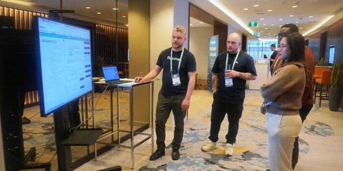 A small group of resolver experts gathered around a screen during a live demo at ascend grc day in toronto. Two team members wearing resolver shirts are presenting software features while attendees observe and engage.