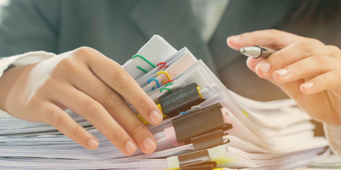 Close-up of hands sorting through stacks of documents and papers, highlighting the detailed process of building an audit plan.
