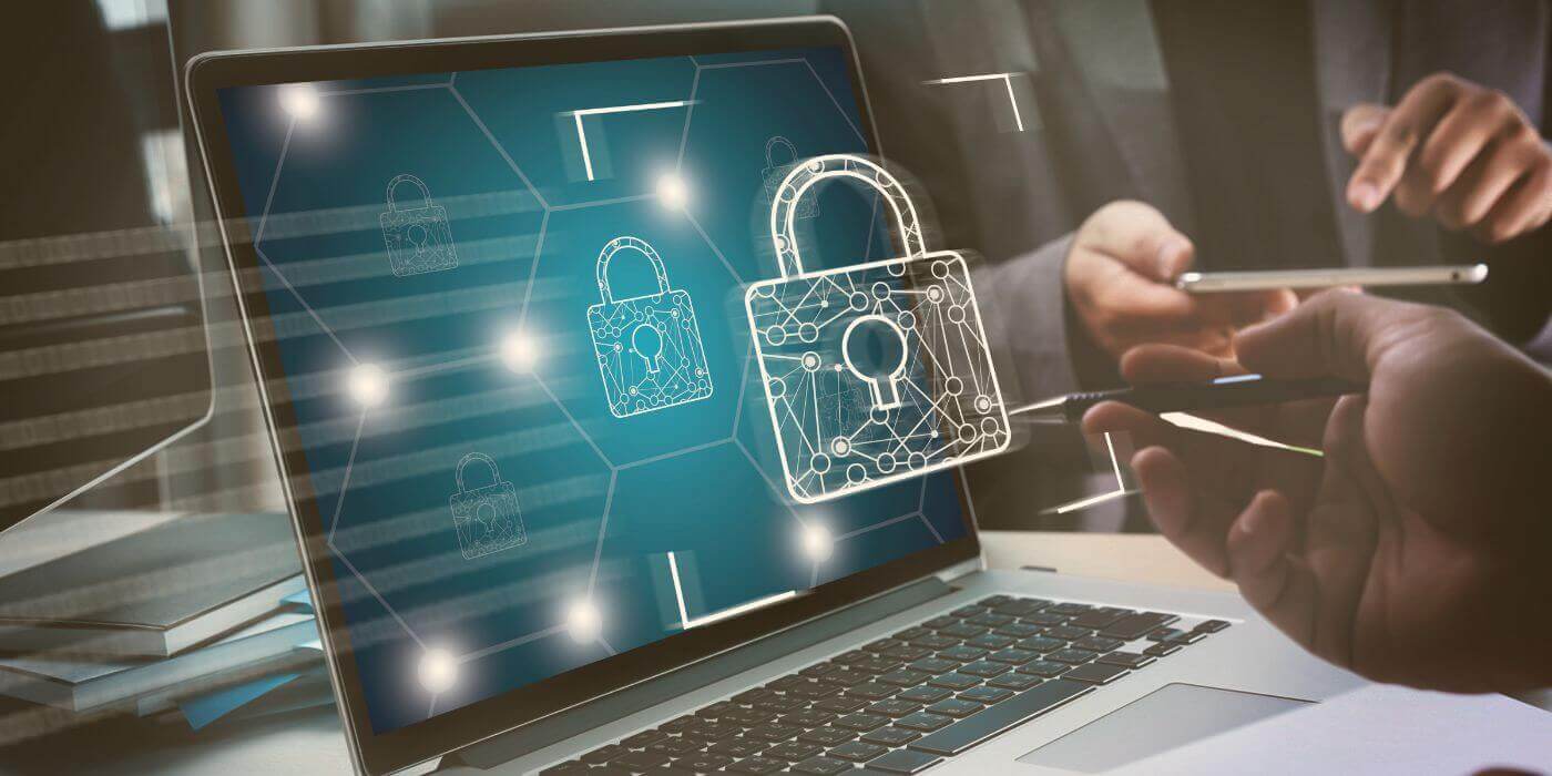 Close-up of a laptop screen displaying digital padlocks, symbolizing cybersecurity and data protection. The screen shows a network with interconnected locks. In the background, two people are seen interacting with a tablet and a pen, suggesting a collaborative work environment focused on security. The overall setting indicates a professional workspace dedicated to ensuring data security and privacy representing physical security programs