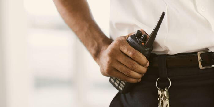 Man holding walkie-talkie secured to his belt behind keychain representing security team risks