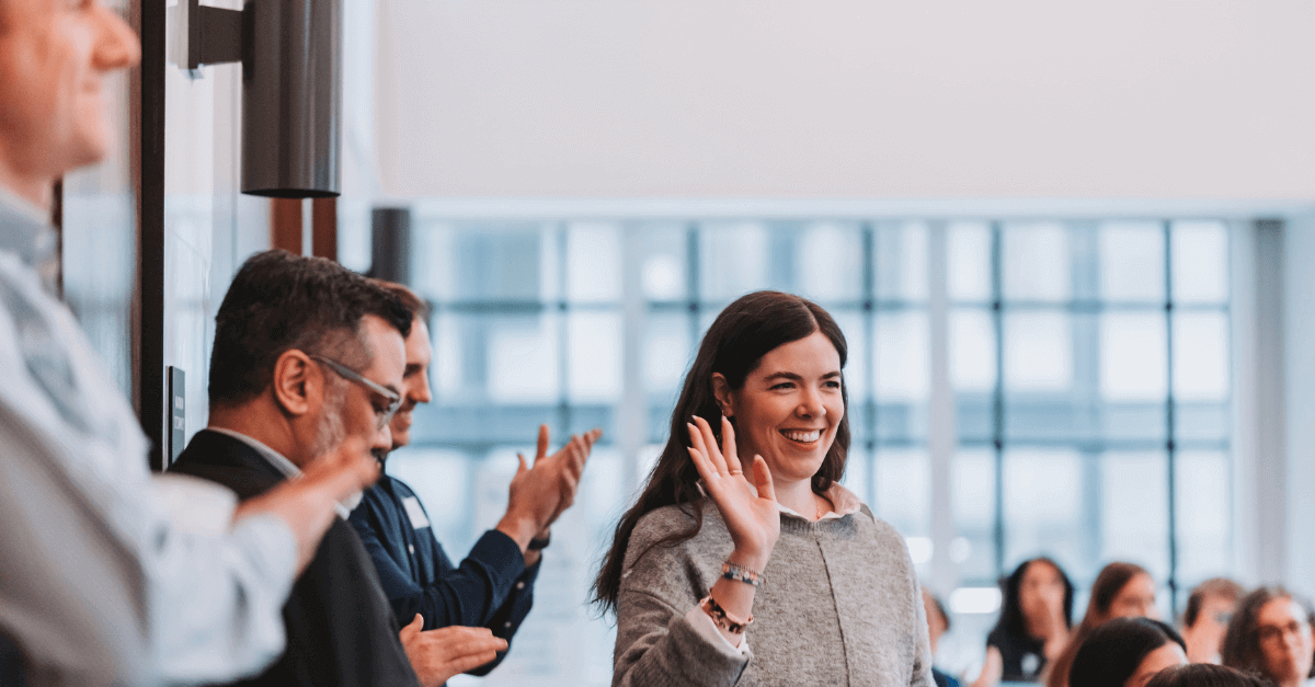 Key insights from resolver's grc day 2024 8 A smiling woman waving in greeting, surrounded by applauding colleagues at a networking event during grc day 2024