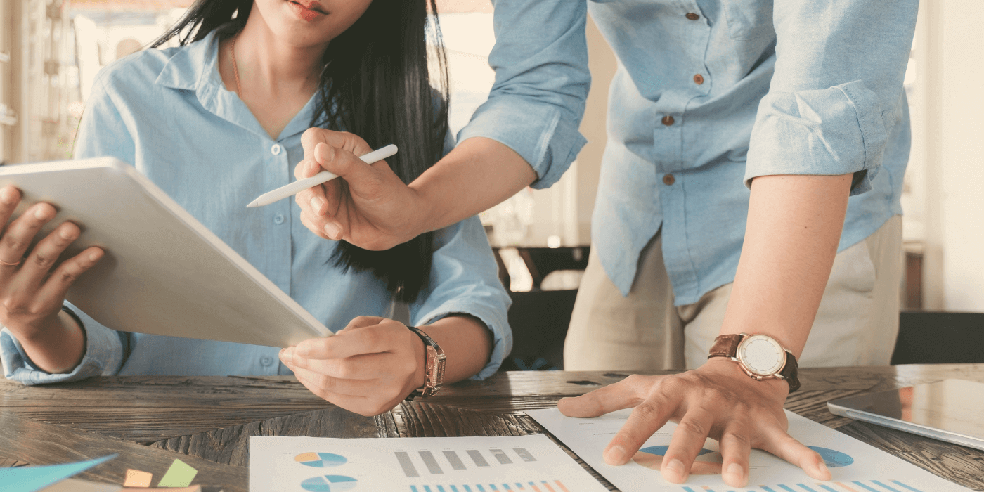 Two professionals evaluating roi in risk management using a digital tablet and paper charts on a wooden table.