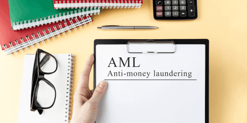 Office desk with a clipboard containing a paper labeled "aml anti-money laundering", a hand pointing to the text, alongside a pair of glasses, assorted notebooks, a pen, and a calculator on a yellow background representing eu anti-money laundering authority